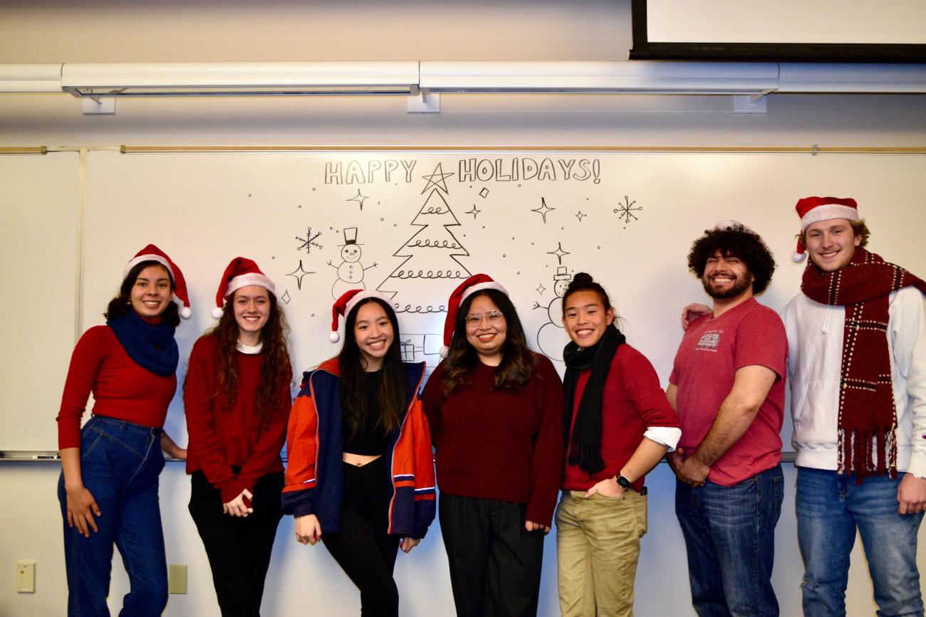 Image of Marketing Messenger team in front of holiday decorated whiteboard. Group is donned in red shirts, scarves, and Santa hats. 